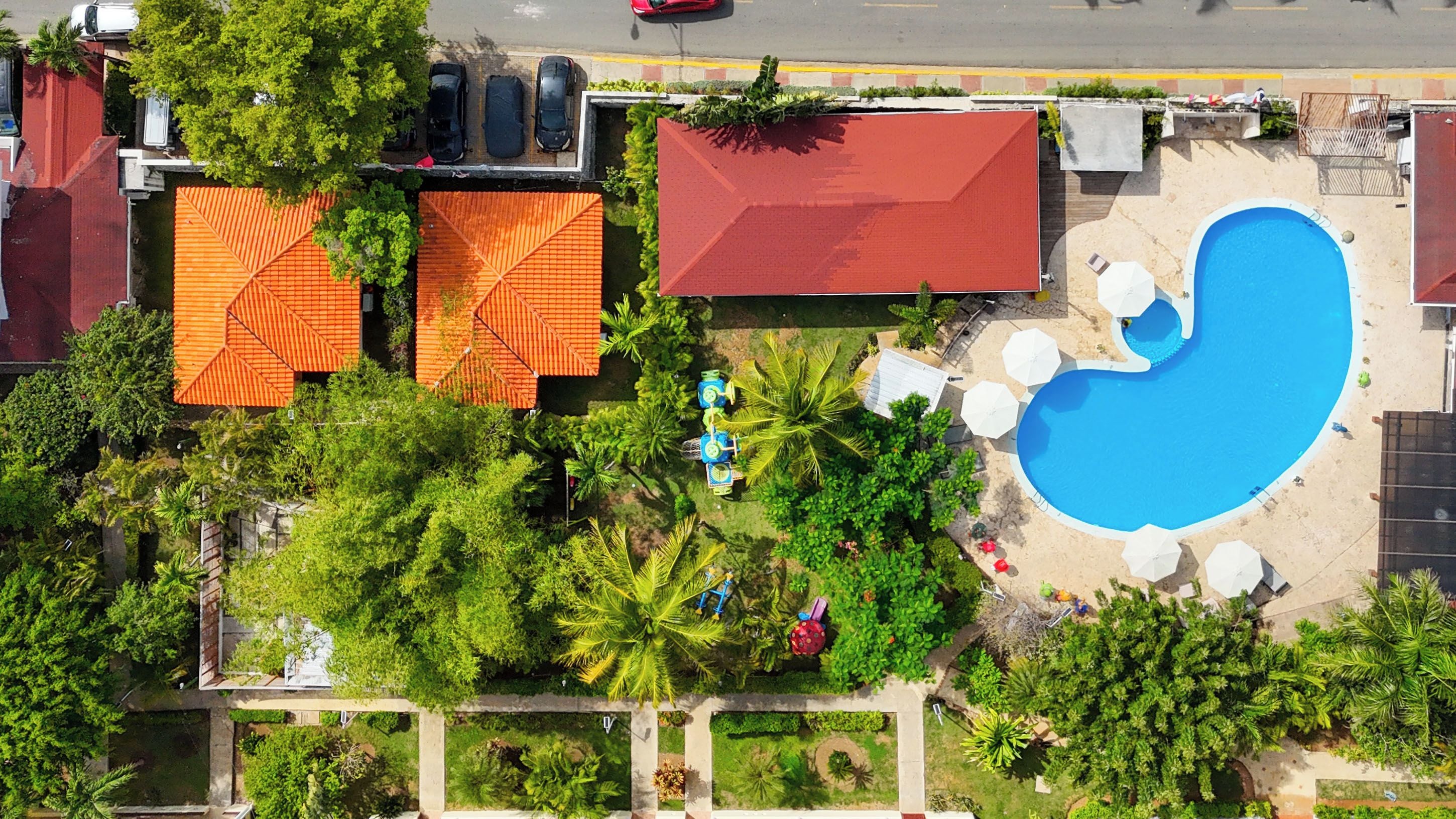 An aerial view of a property with a swimming pool, multiple buildings with red roofs, and lush greenery.
