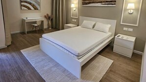 Quarto moderno com cama grande, mesas de cabeceira, escrivaninha e obras de arte nas paredes.