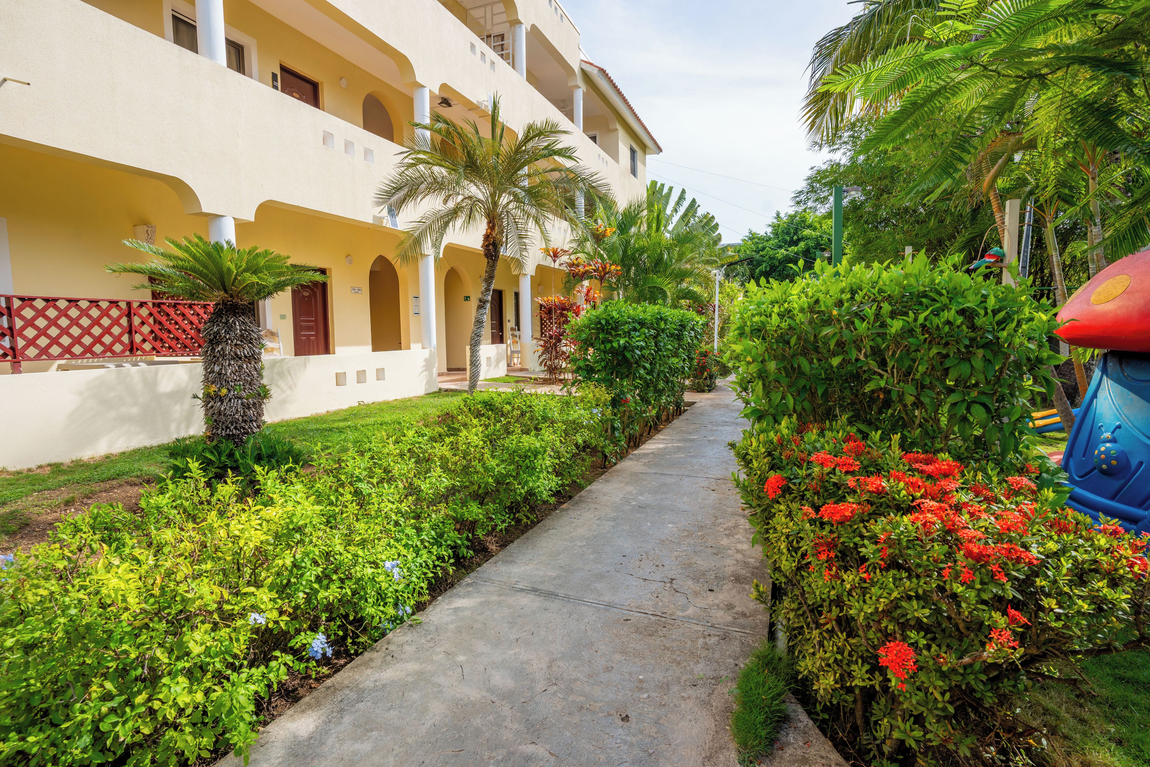 A pathway flanked by lush greenery and a building with multiple balconies.