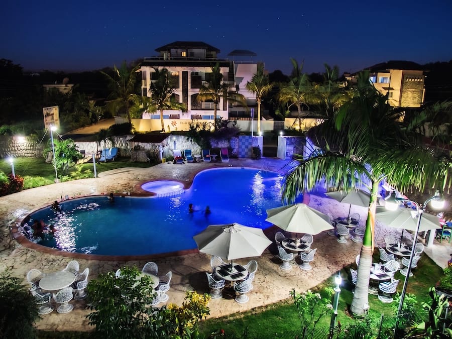 A nighttime view of a resort with a swimming pool, lounge chairs, and a building with a sign.