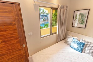 Un dormitorio con puerta de madera, ventana con cortinas, cama con ropa de cama estampada y un cuadro en la pared.