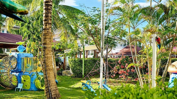 A playground with slides and climbing structures, surrounded by lush greenery and palm trees. - Casual Eden Bayahibe by Casual Hoteles (Dominicus)