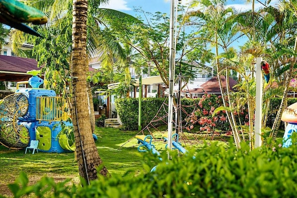 A playground with slides and climbing structures, surrounded by lush greenery and palm trees. - Casual Eden Bayahibe by Casual Hoteles (Dominicus)
