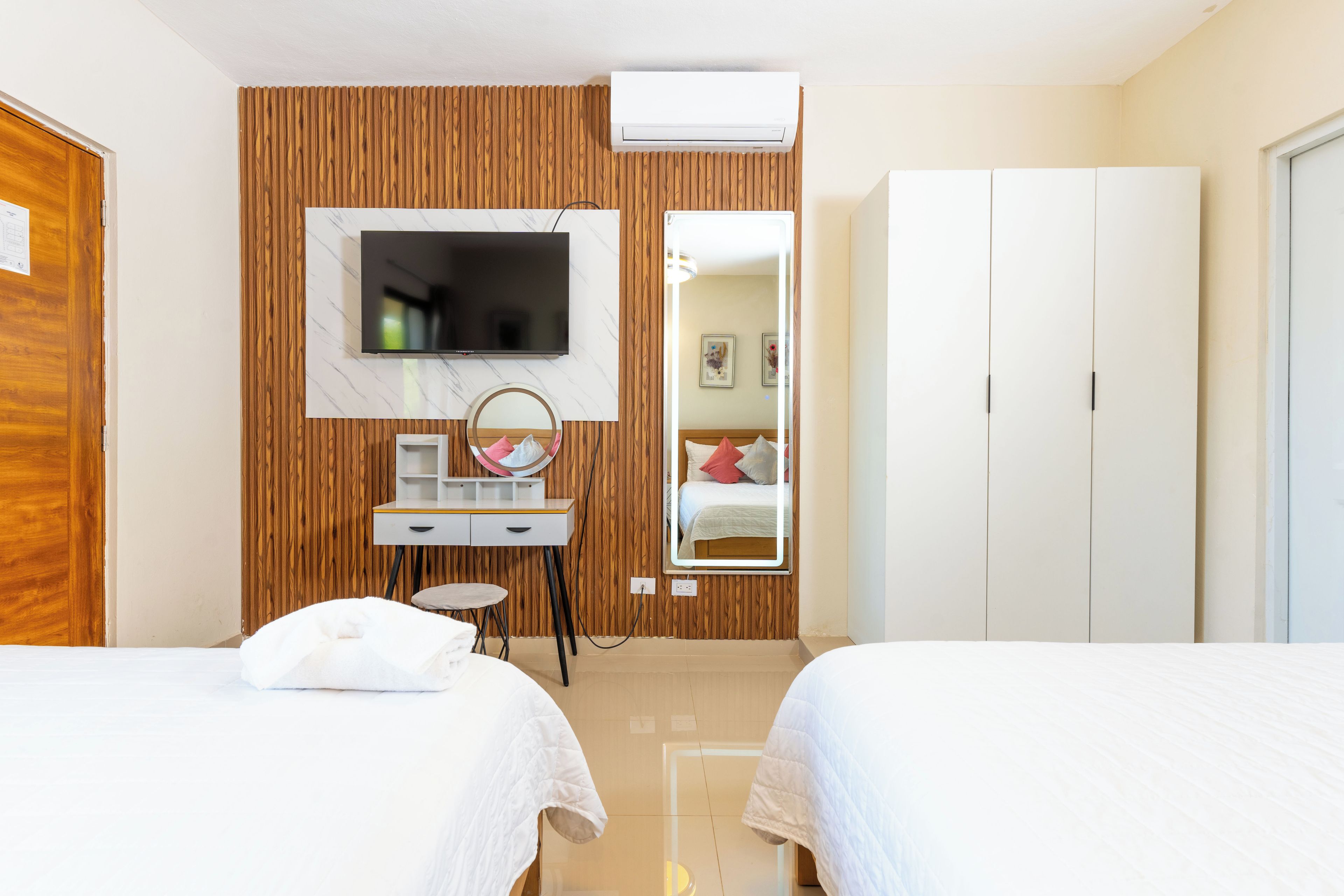 A hotel room with two beds, a TV, a mirror, a desk, and a wardrobe.
