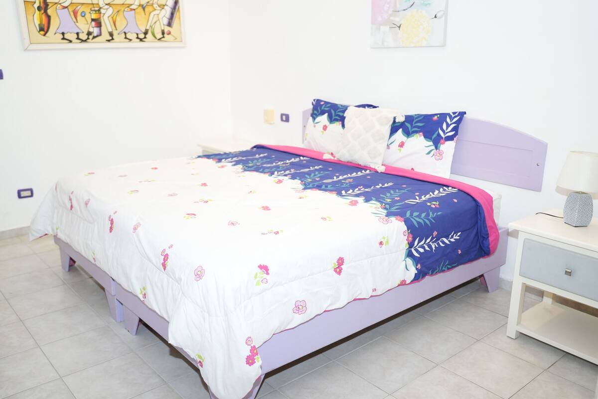 A bedroom with a bed, a nightstand, and a wall-mounted lamp.