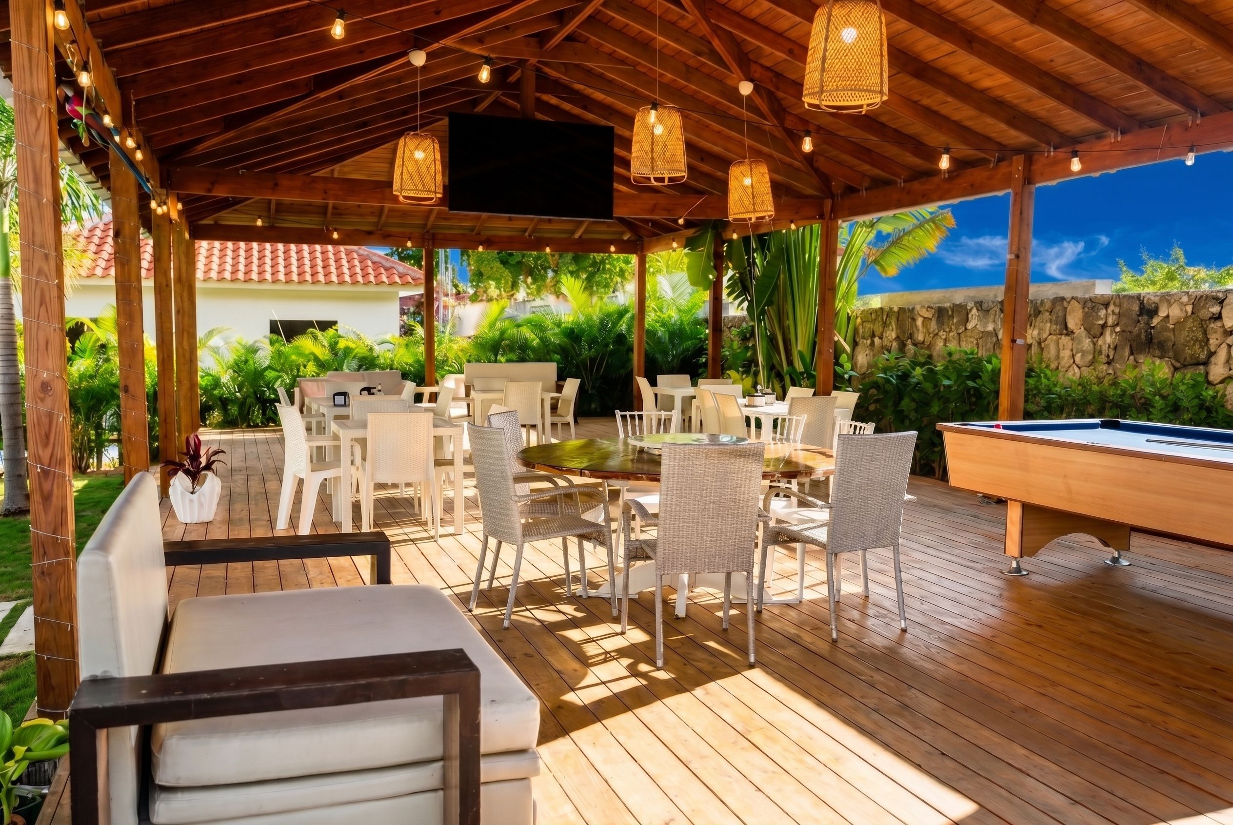 Un patio al aire libre con suelo de madera, muebles blancos y una mesa de billar.