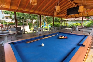 Un área de piscina al aire libre con mesa de billar azul, sillas de descanso y una zona de juegos infantiles.