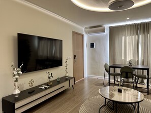Una sala de estar moderna con un televisor de pantalla plana, una mesa de comedor con sillas, un sofá y una mesa baja.