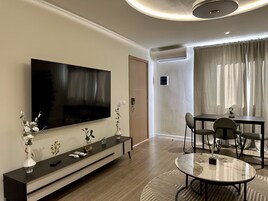 A modern living room with a flat-screen TV, a dining table with chairs, a sofa, and a coffee table.