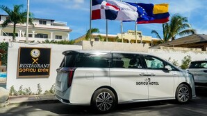Uma minivan branca com a marcação 'SOFICU HOTEL' estacionada em frente a um edifício com uma placa que diz 'RESTAURANTE SOFICU EDEN'.