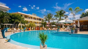 A swimming pool with lounge chairs and palm trees, surrounded by a hotel building.