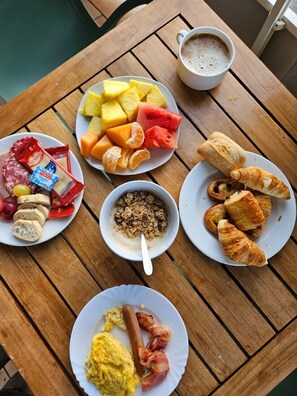 Una mesa de desayuno con platos de comida, incluyendo croissants, fruta y huevos revueltos.