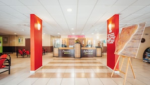 Un área de recepción con mostrador de registro, pilares rojos y un cuadro sobre caballete.