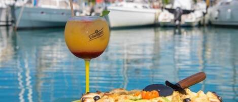 A pizza with a pizza cutter on a green cutting board, a glass of drink with a straw, and a pair of sunglasses on a green surface.