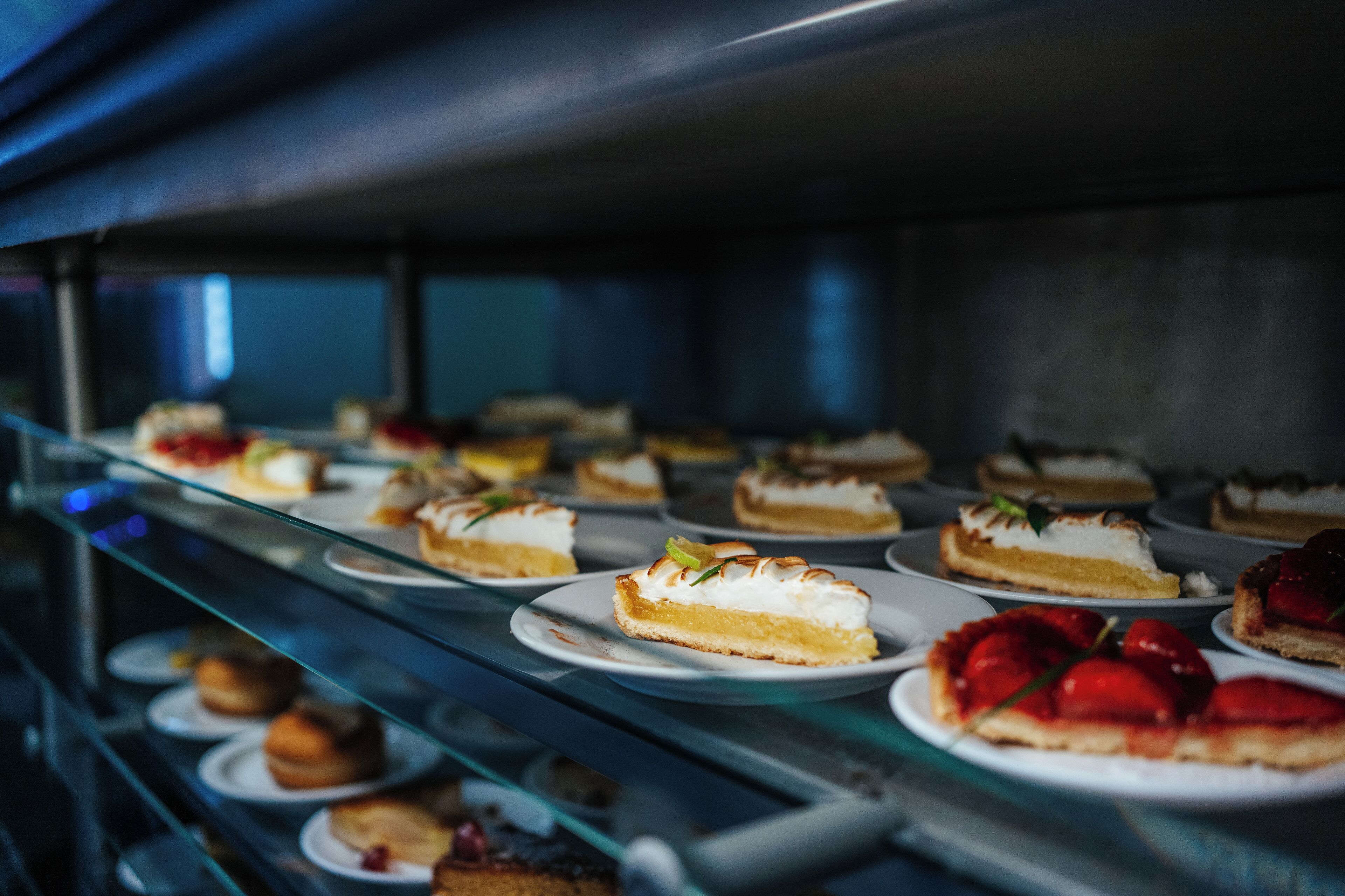 A display case with various desserts, including cakes and pastries, arranged on plates.