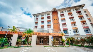 Un hotel de varios pisos con una entrada destacada, palmeras y cielo despejado.