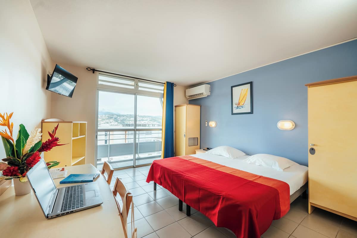 Habitación de hotel con cama, escritorio con computadora portátil, ventana con vistas y televisor montado en la pared.