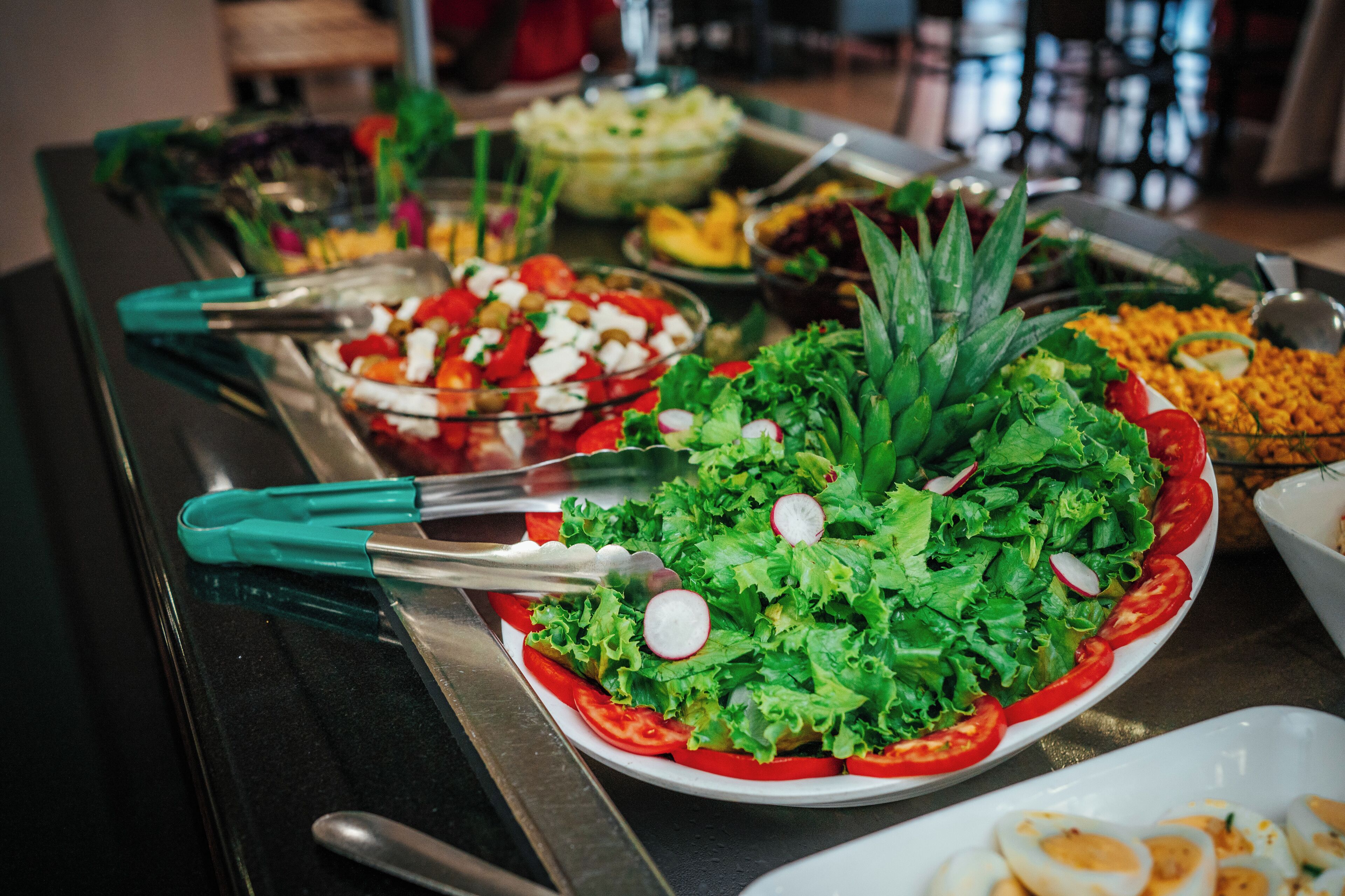 Une table de buffet proposant divers plats, notamment des salades, des fruits et une assiette d’œufs durs.