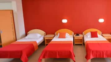 Camera d'albergo con tre letti singoli, ognuno con copripiumino rosso e cuscini bianchi. Due comodini con lampade e pareti dipinte di rosso.
