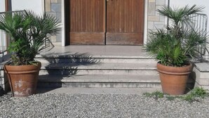 Entrada de un edificio con una puerta doble de madera, dos macetas a cada lado y un camino de grava.