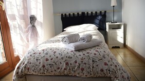 Una cama bien tendida con ropa de cama floral, una lámpara de noche y vistas al exterior a través de una ventana.
