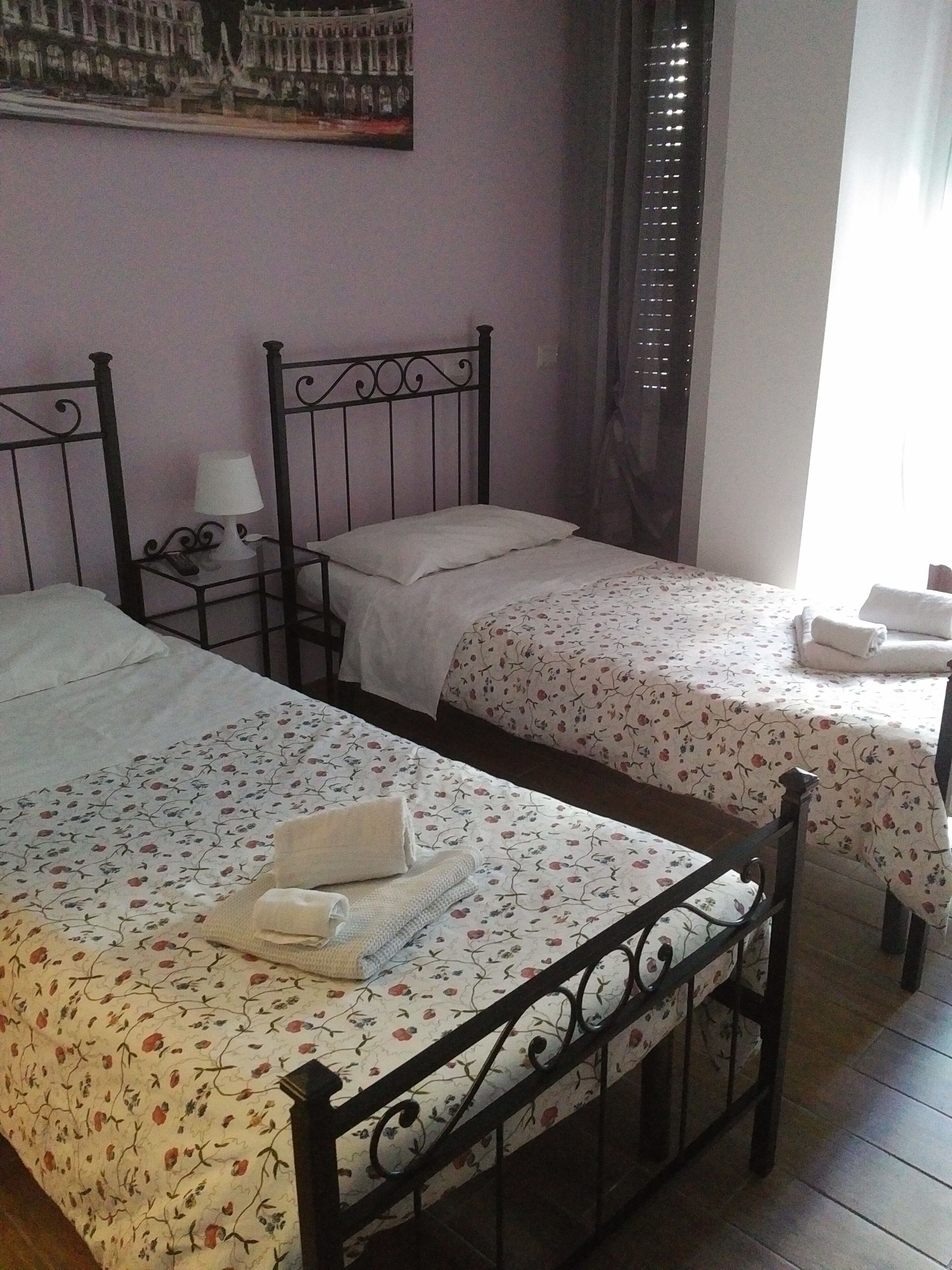 Habitación de hotel con dos camas individuales, cada una con una colcha estampada y un cojín blanco. Entre las camas hay una mesita con una lámpara.