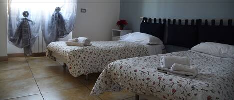 A hotel room with two beds, a nightstand, a potted plant, and a window with sheer curtains.