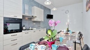 Una cocina moderna con armarios blancos, horno integrado y una zona de comedor con una mesa dispuesta para dos.