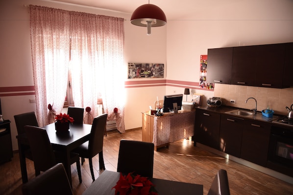 A compact kitchen with a dining area, wooden cabinets, a small island, and a pendant light. - Marco e Laura B&B (Rome)