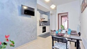 Cocina moderna con armarios blancos, horno integrado y un comedor con mesa y sillas.