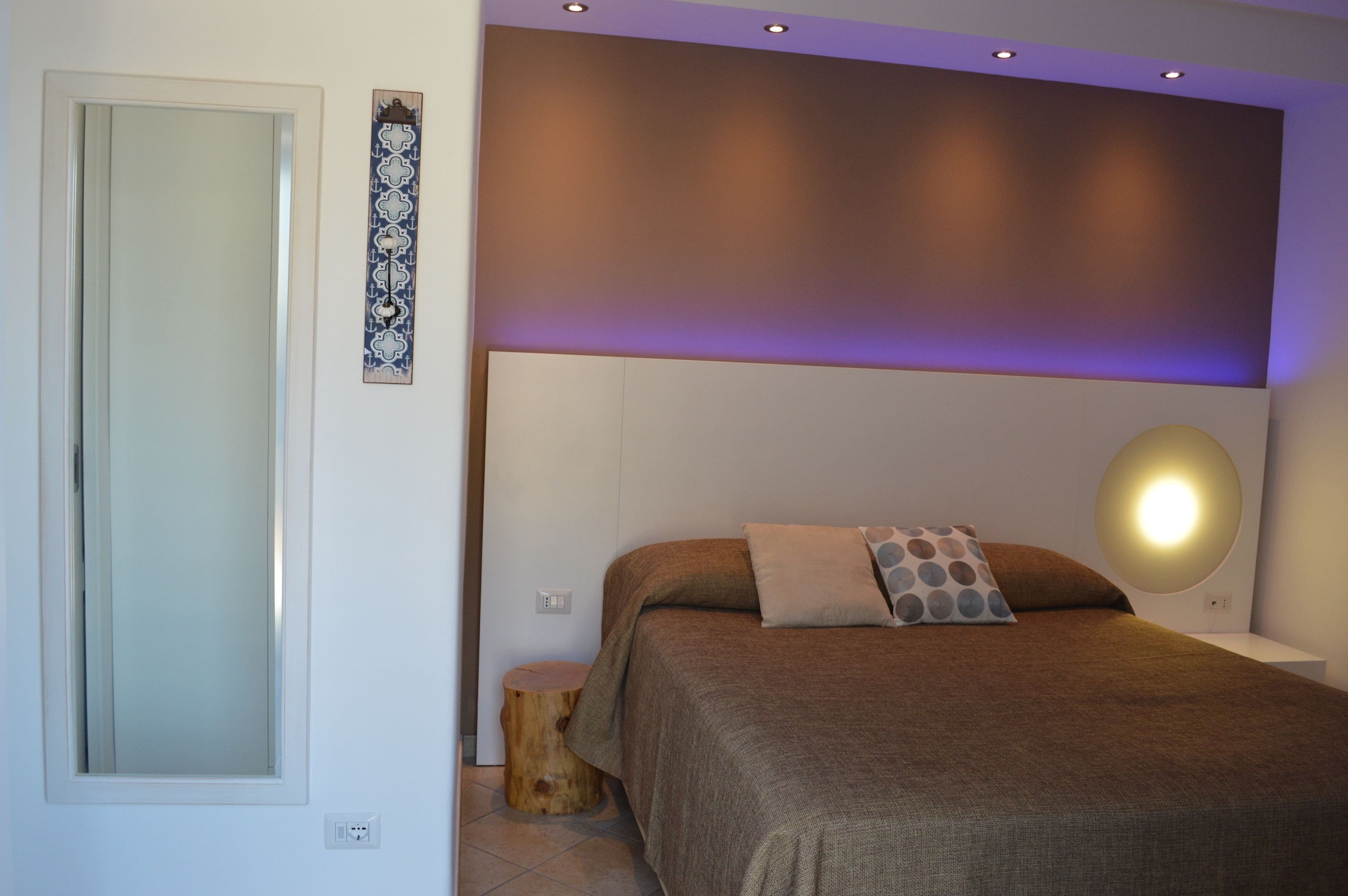 A bedroom with a bed, bedside tables, a wall-mounted light, and a decorative wall piece.