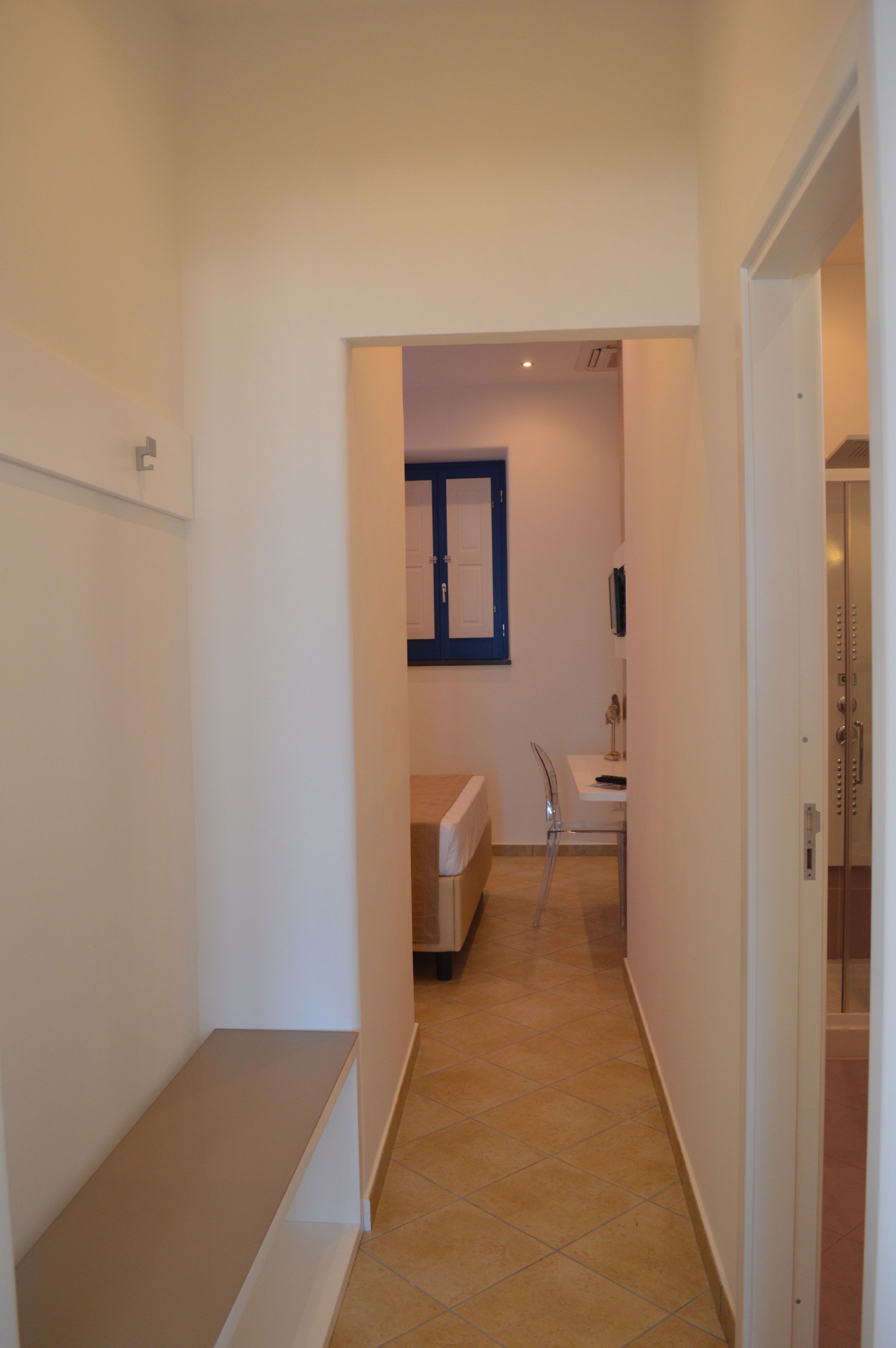 Un couloir étroit, avec un banc sur le côté gauche, qui mène à une salle de bain équipée d’un miroir et d’un lavabo.