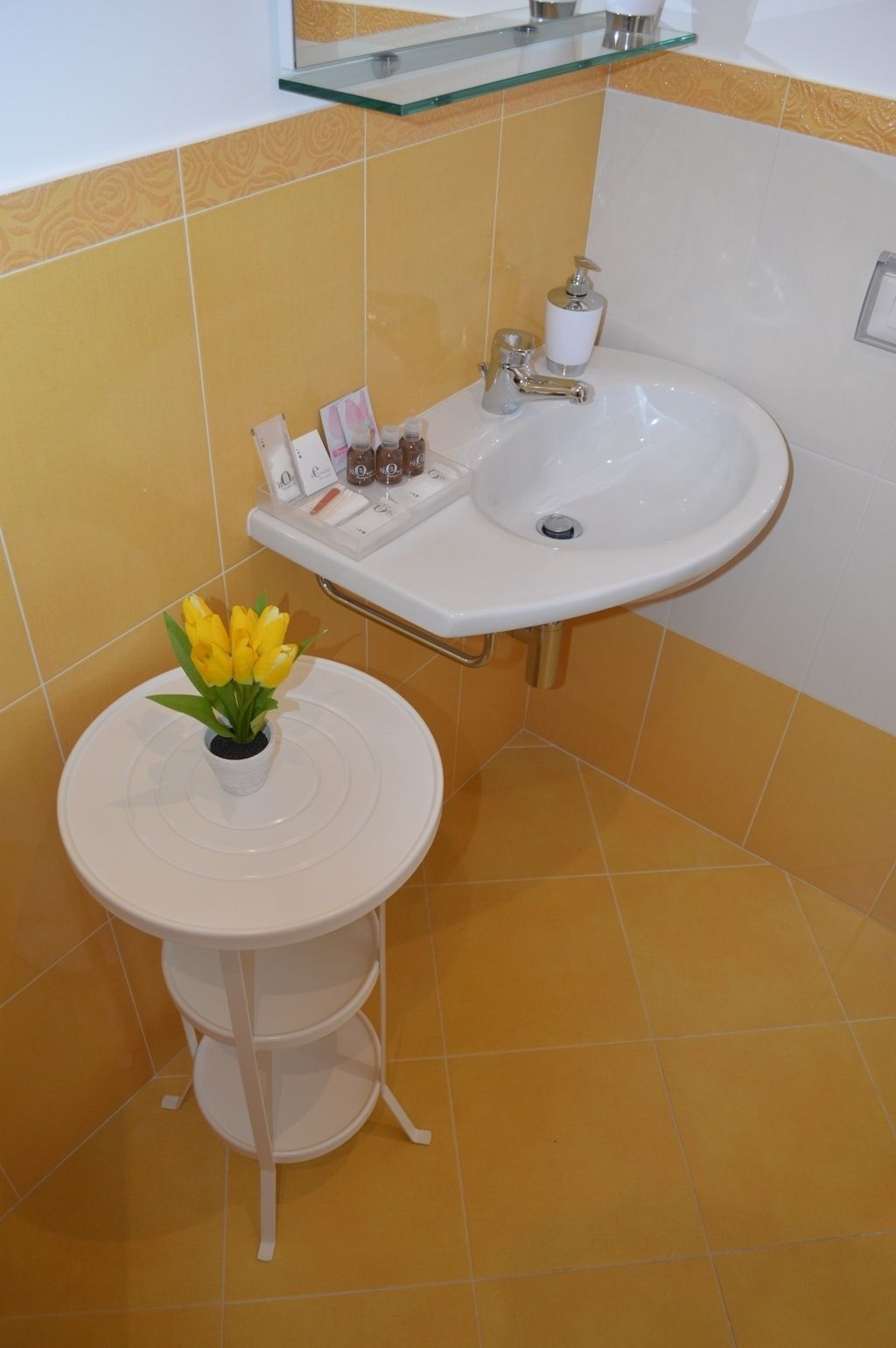 A bathroom with a sink, a small table with a flower vase, and toiletries on the sink.