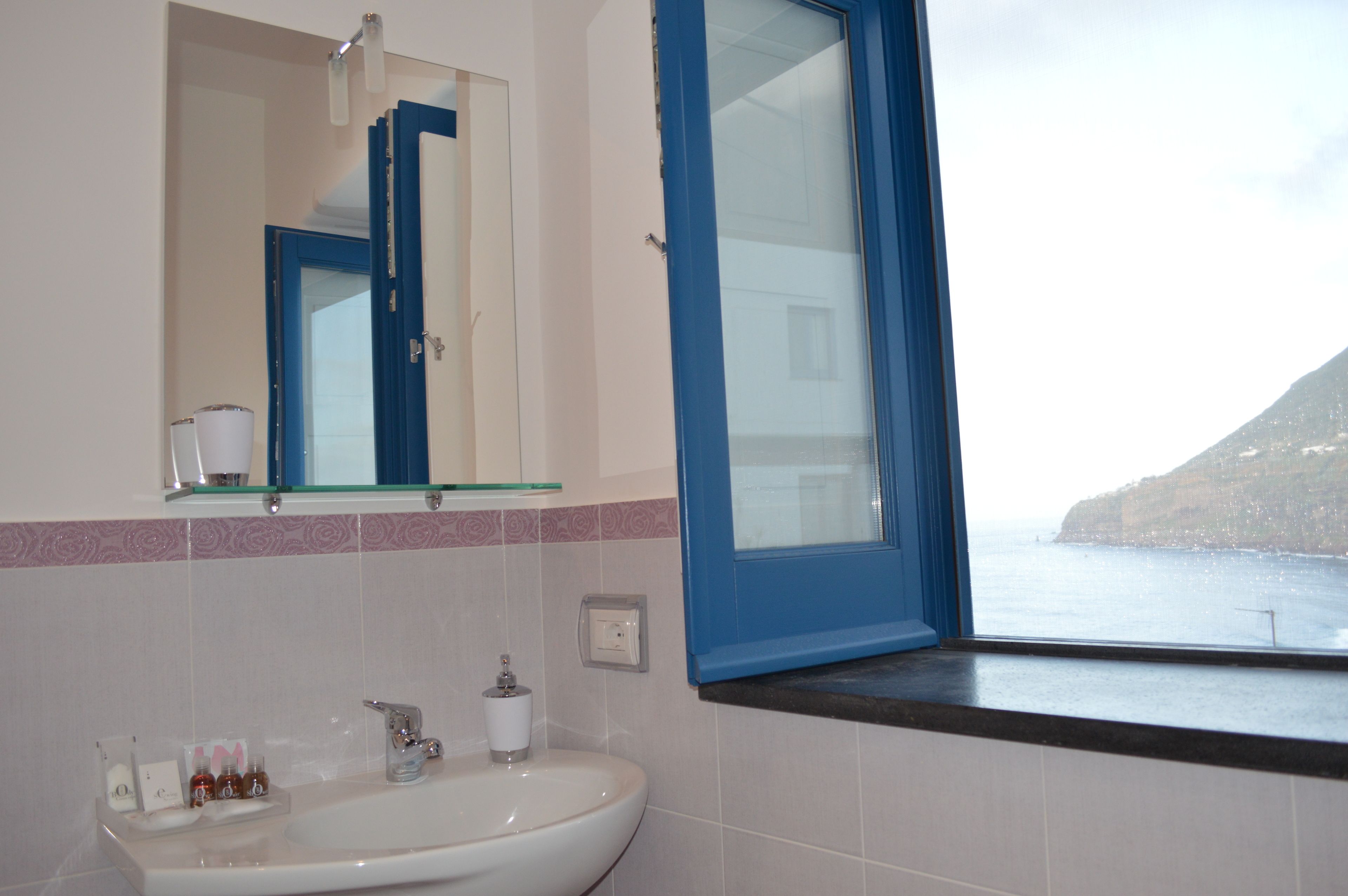 A bathroom with a sink, mirror, and window overlooking a coastal view.