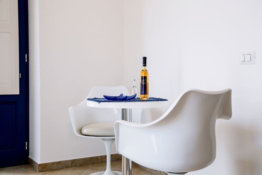Een moderne eethoek met een witte tafel, een blauwe schaal, een wijnfles en een witte stoel.