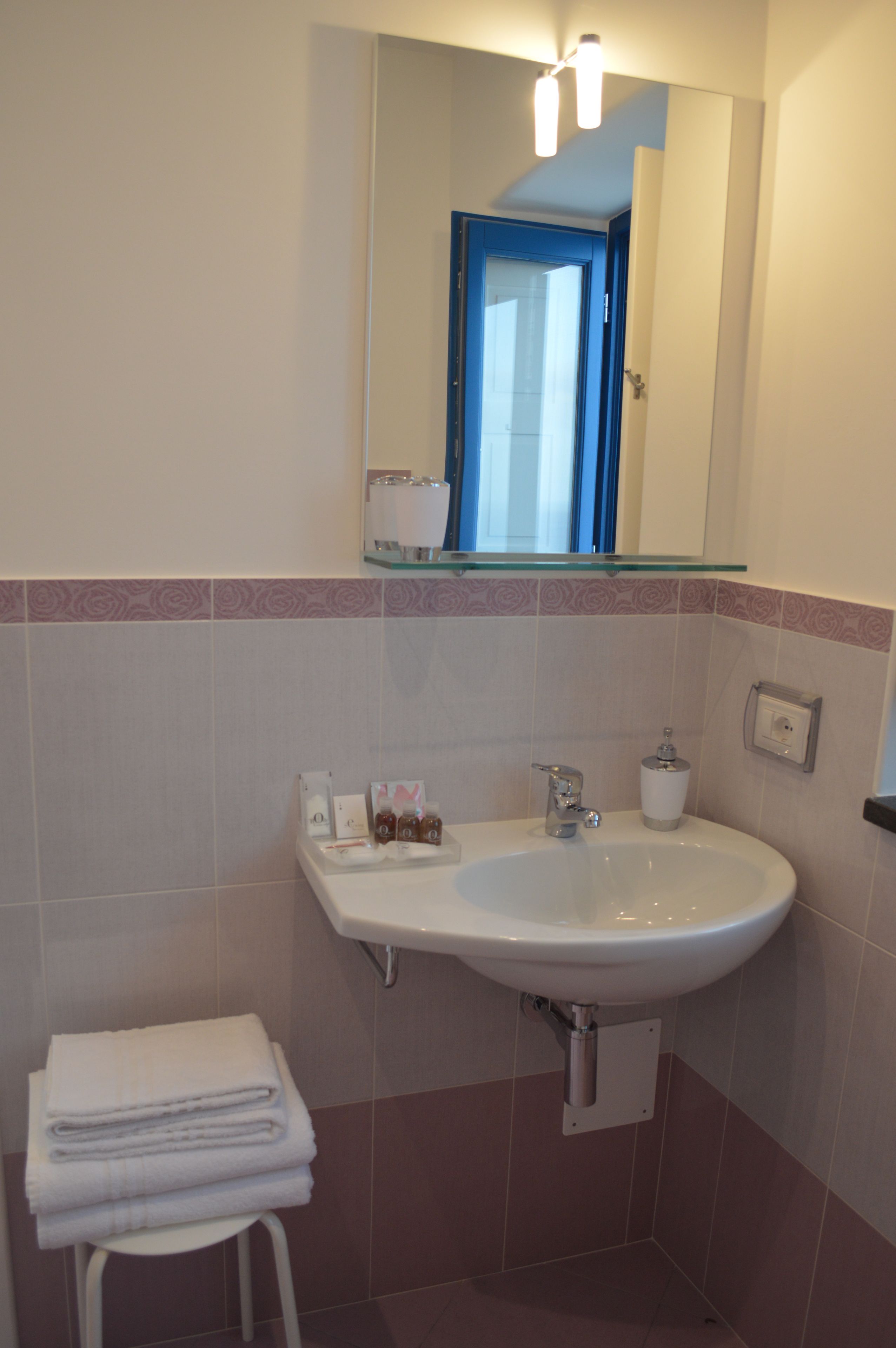 Un baño con un lavamanos blanco, un estante de vidrio arriba y un espejo que refleja una puerta.