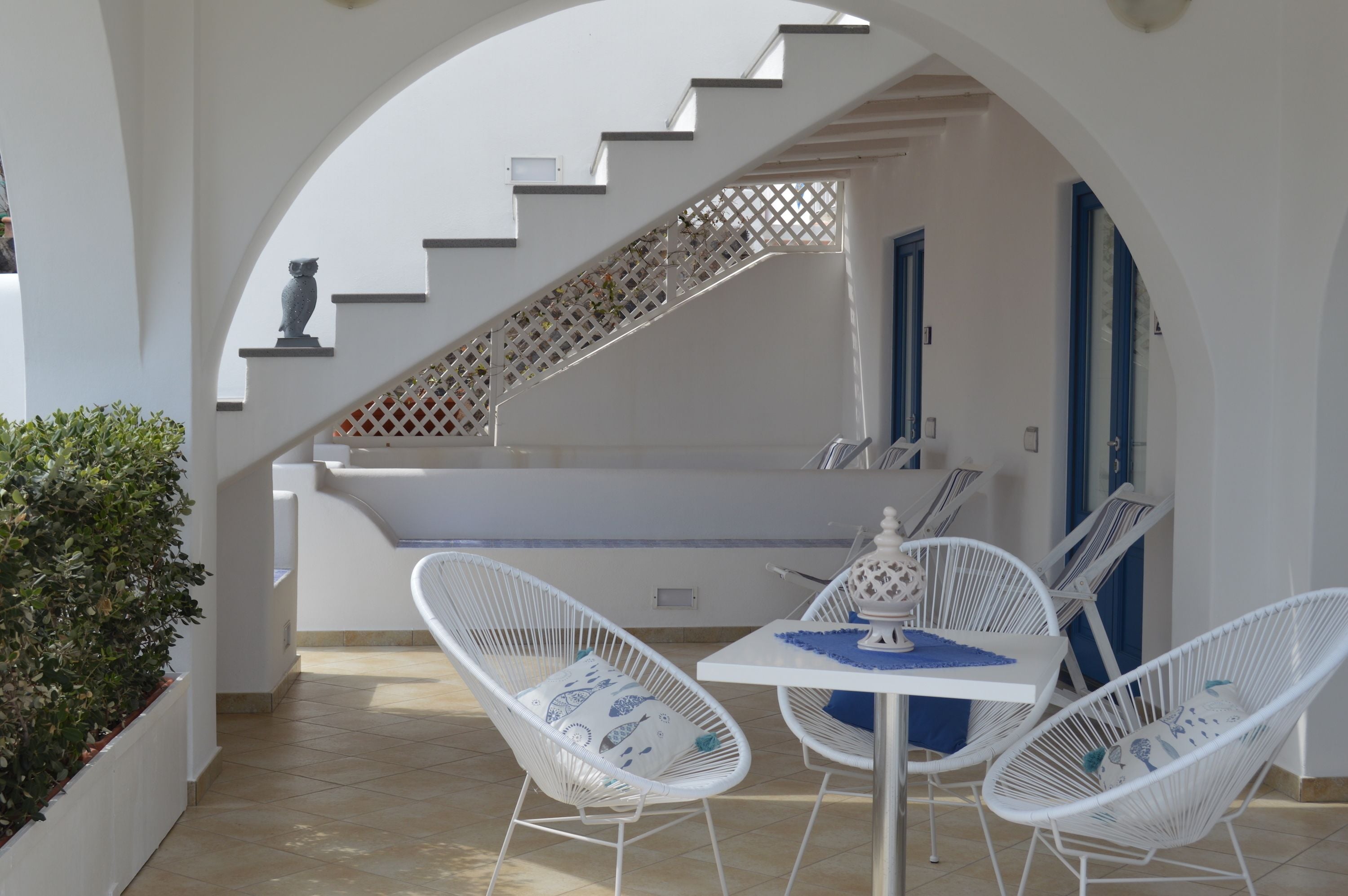 Um pátio exterior branco com mesa, cadeiras, escadas e uma porta.