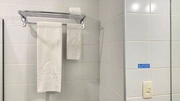 Un baño con paredes de azulejos blancos, un perchero con dos toallas y un cartel que indica que el agua está caliente.