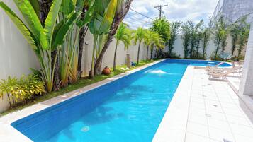 Une piscine rectangulaire dont les bords sont recouverts de carreaux, entourée de plantes tropicales et de palmiers.
