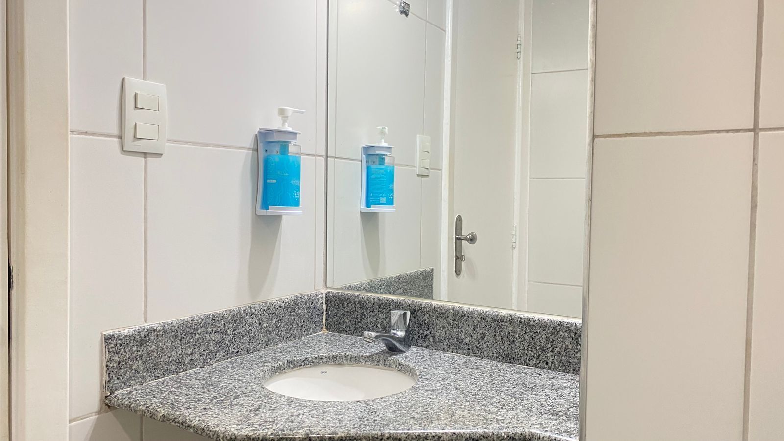 A bathroom with a granite countertop sink, a mirror, and two blue soap dispensers mounted on the wall.