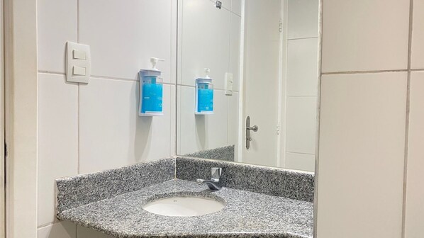 Un baño con lavamanos de encimera de granito, un espejo y dos dispensadores de jabón azules fijos a la pared.