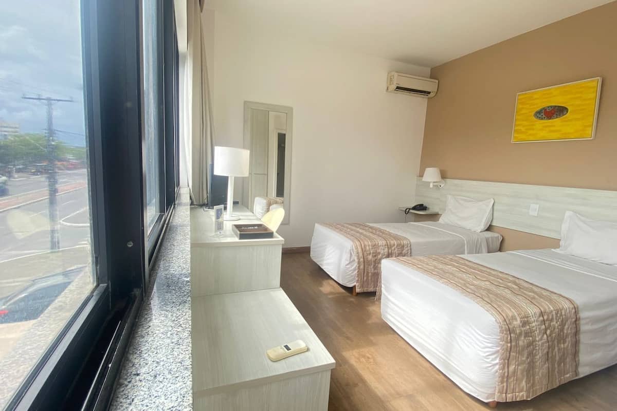 Habitación de hotel con dos camas, un escritorio, una silla, una lámpara y una ventana que da a la calle.