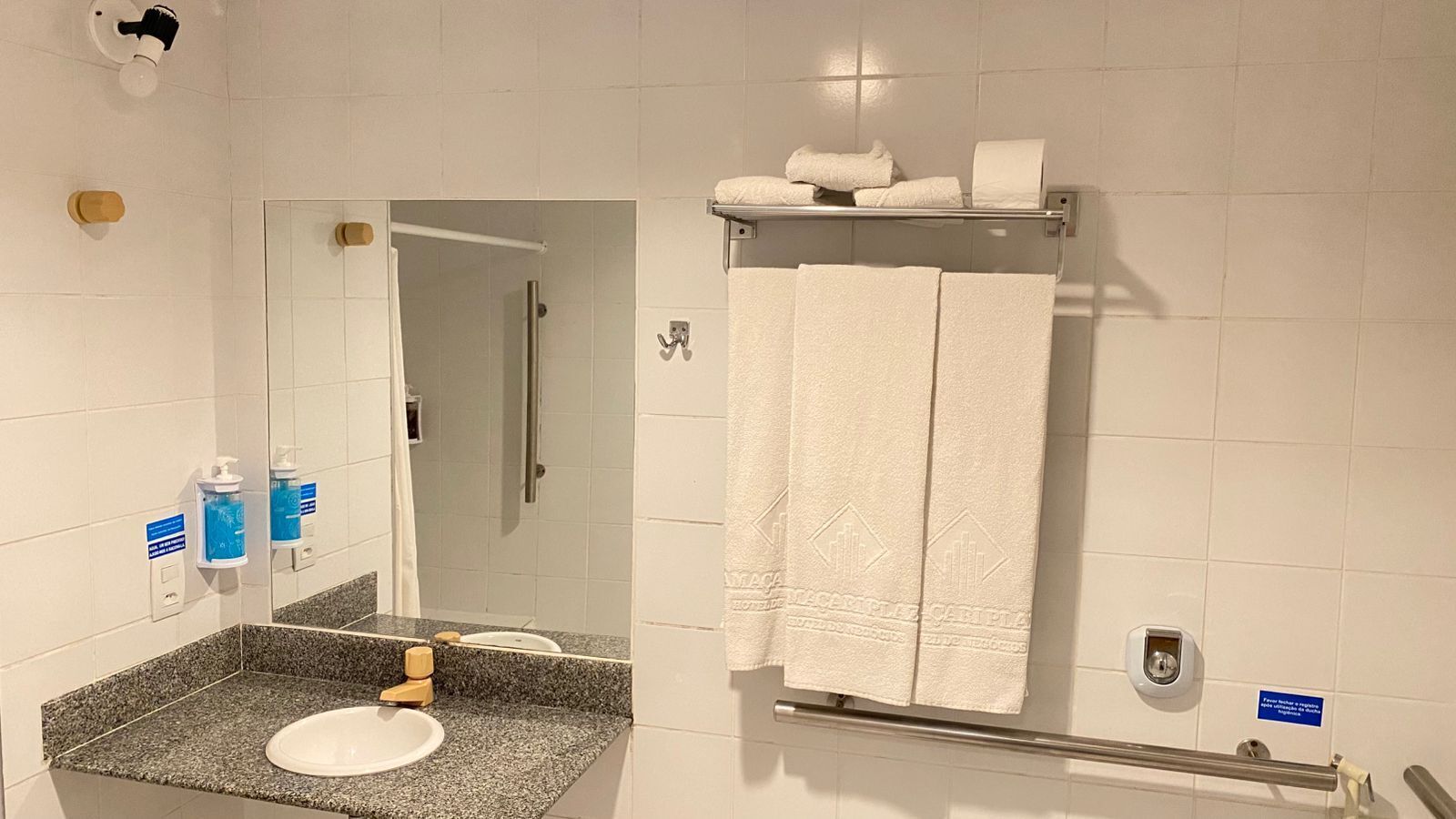 Un baño con lavamanos de encimera de granito, un espejo, toallero con toallas y un secador de manos.