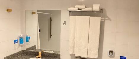 Un baño con lavamanos de encimera de granito, un espejo, toallero con toallas y un secador de manos.