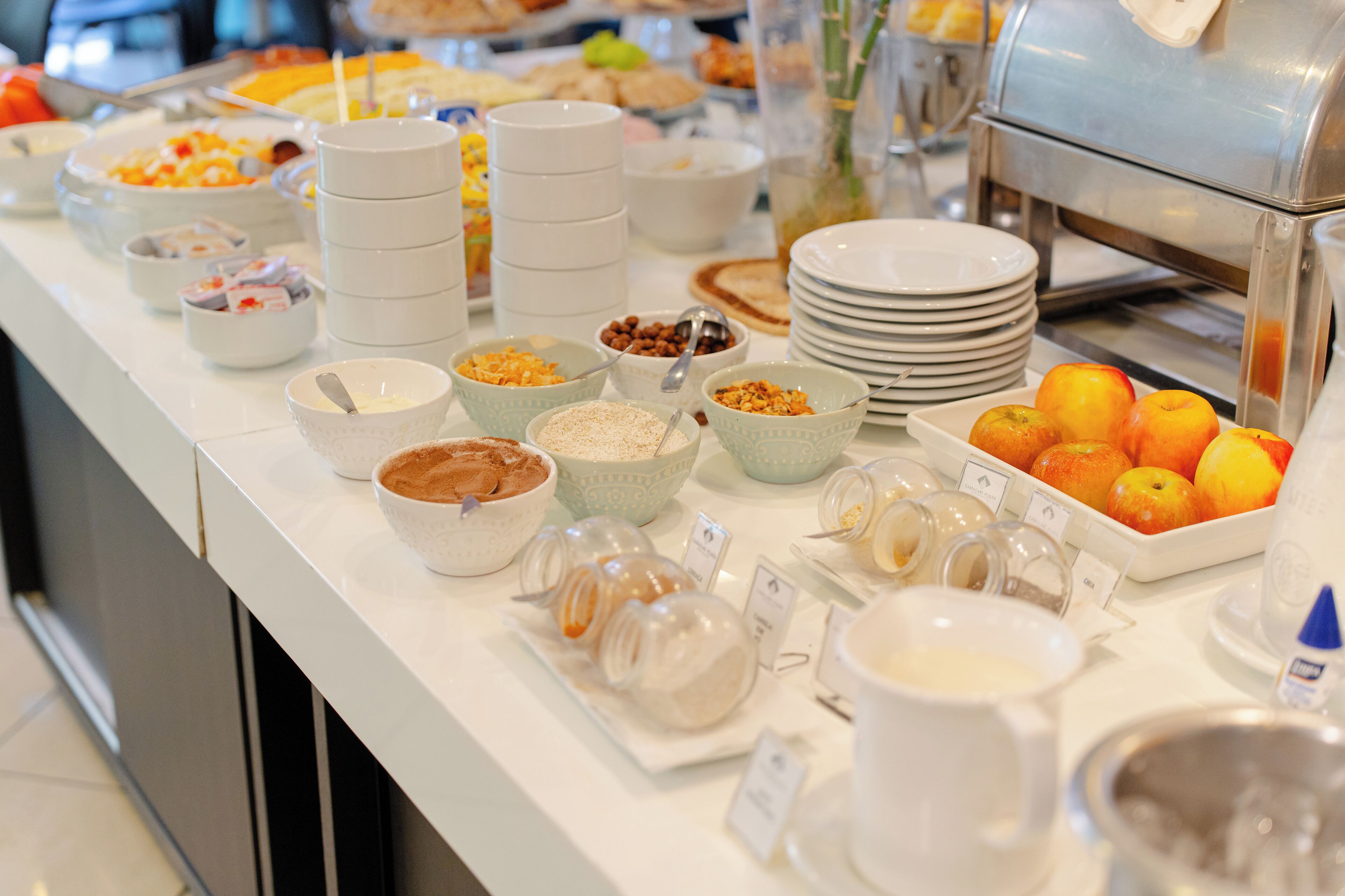 Un bufé con diversos alimentos y recipientes, incluyendo tazones de cereal, frutas y salsas.