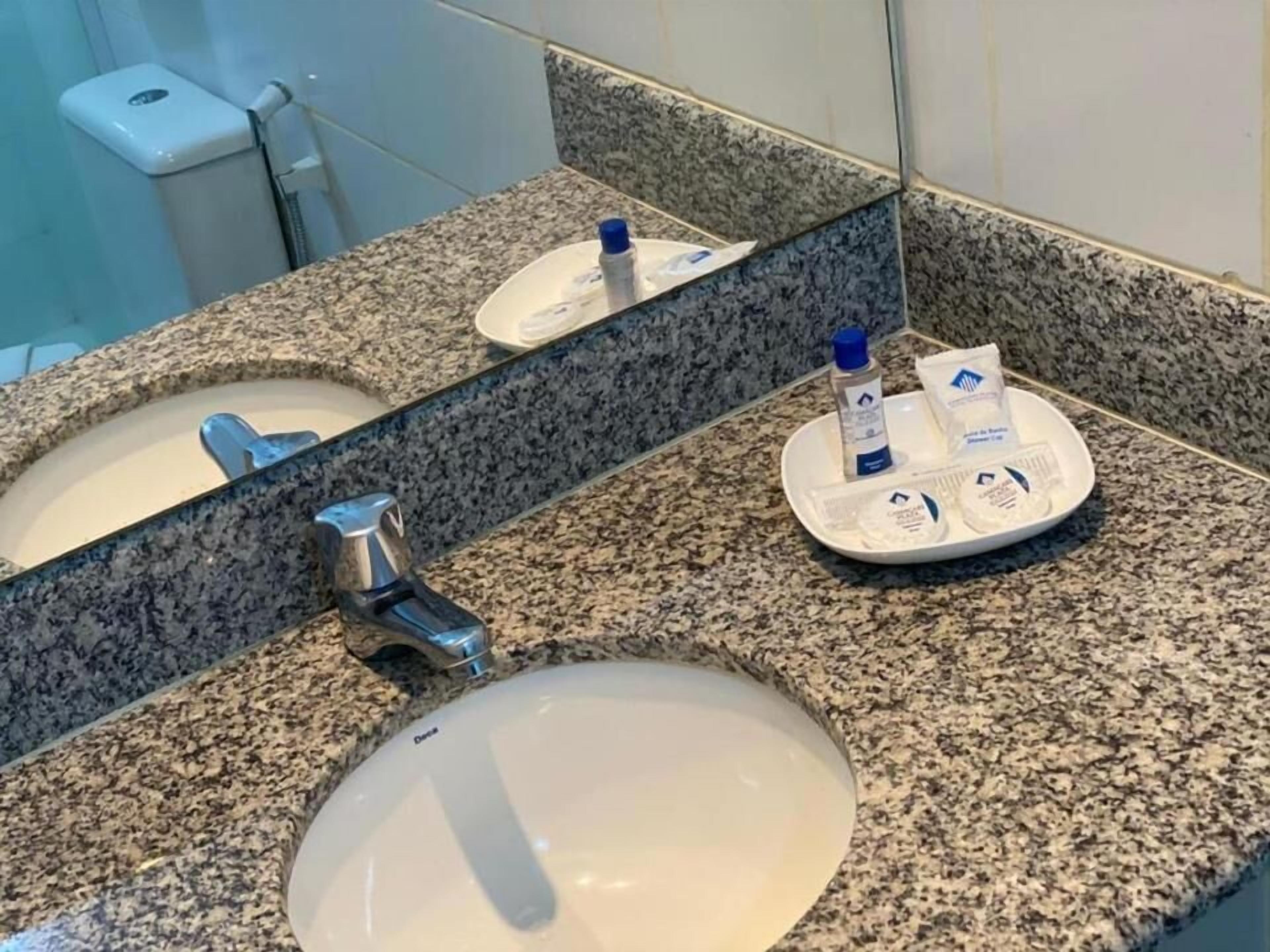 Un baño con encimera de granito, un lavamanos, un espejo y artículos de tocador sobre la encimera.