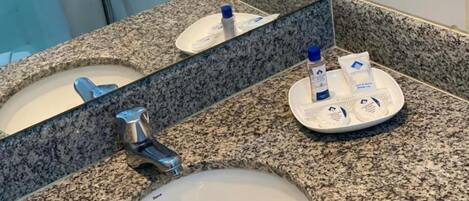 A bathroom with a granite countertop, a sink, a mirror, and toiletries on the counter.