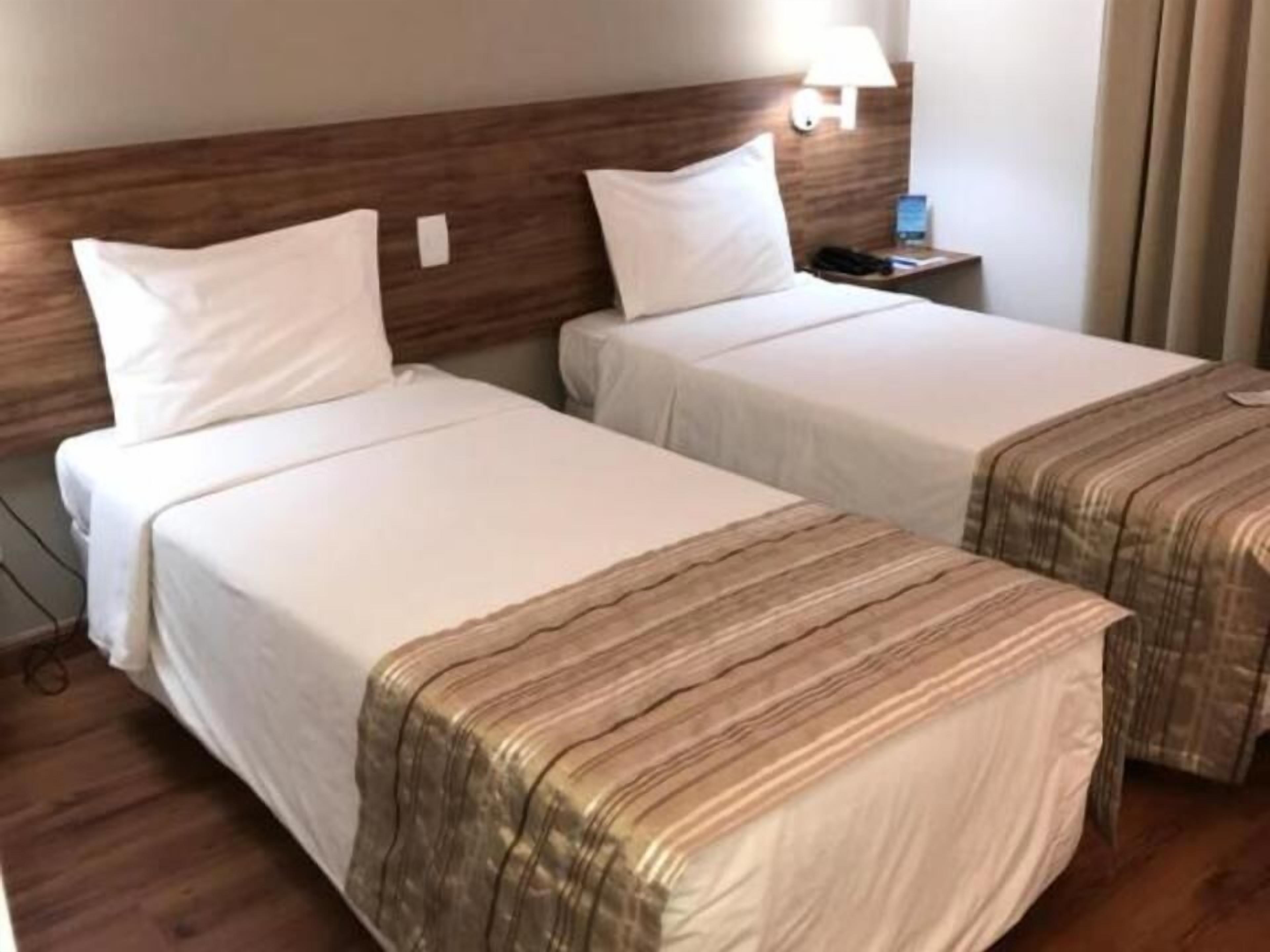 Two single beds with white bedding and striped covers, a wooden headboard, a bedside table with a lamp, and a telephone.
