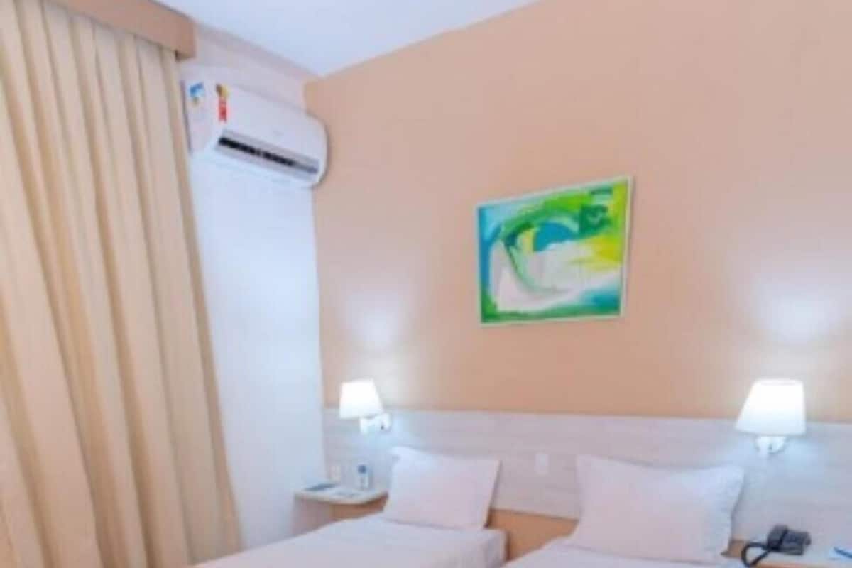 Habitación de hotel con dos camas, un cuadro en la pared, un equipo de aire acondicionado y piso de madera.
