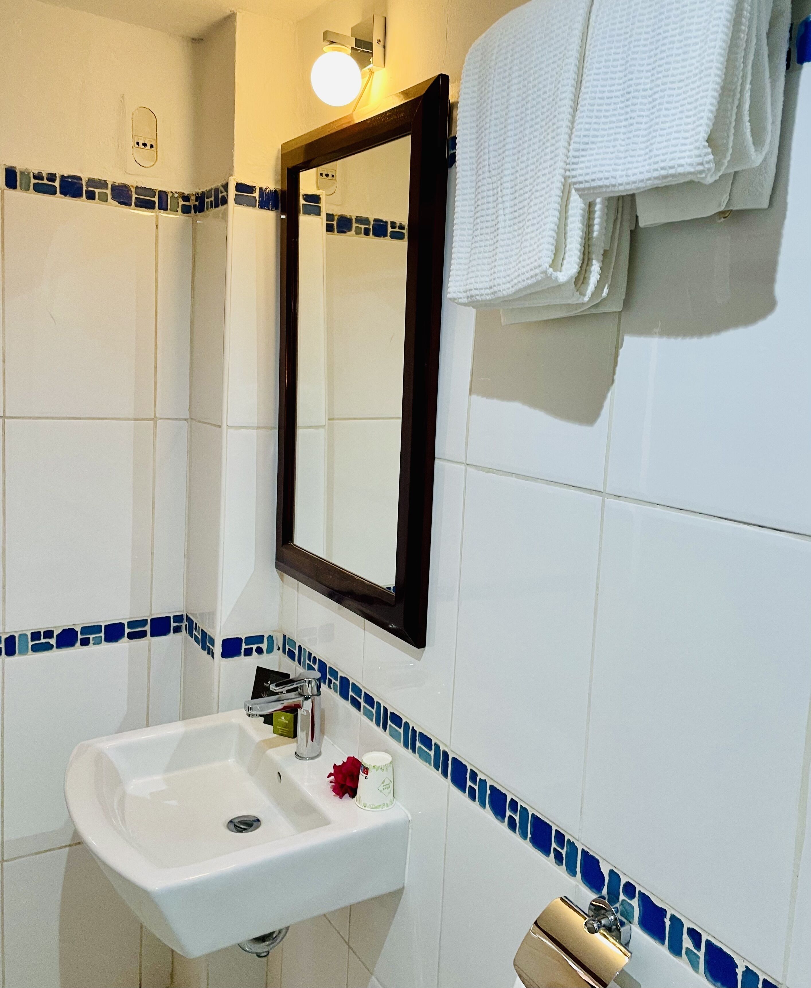 Een badkamer met een witte wastafel, een spiegel en blauwe mozaïektegels.